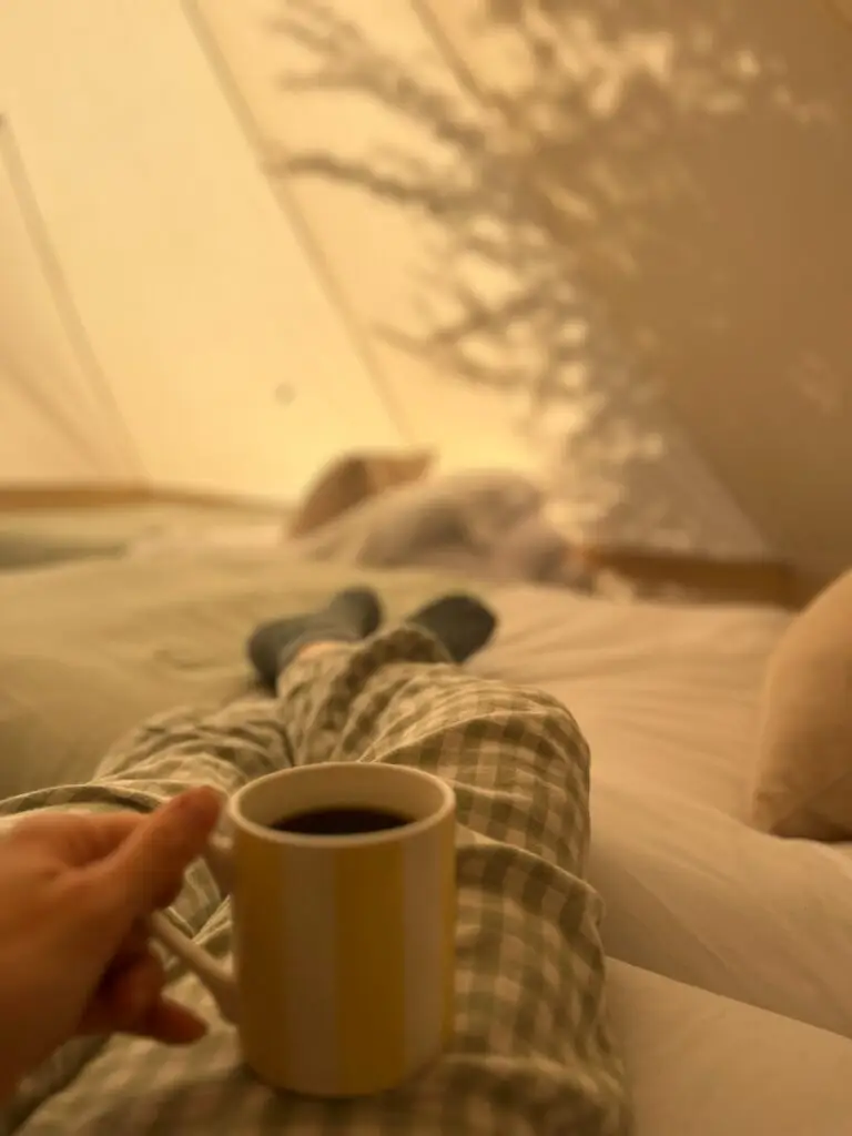 A mug of coffee in bed inside a bell tent