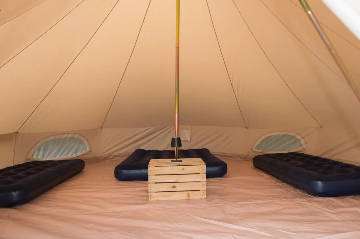 Two single airbeds and a double airbed inside a bell tent, with a crate side table