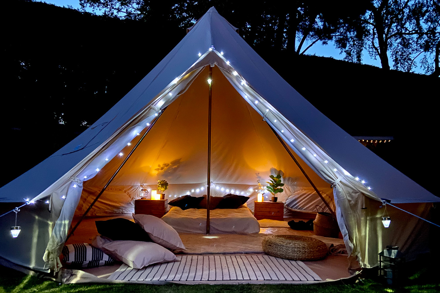 Bell tent lit up warm at night, bed made up inside