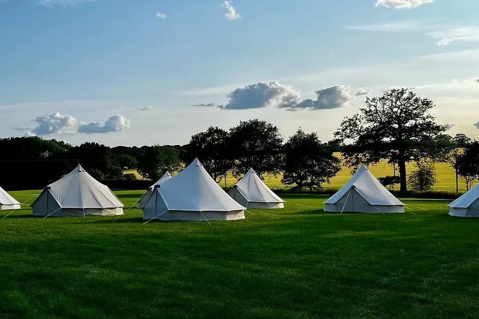 Bell tents spread across a green field in the evening sun