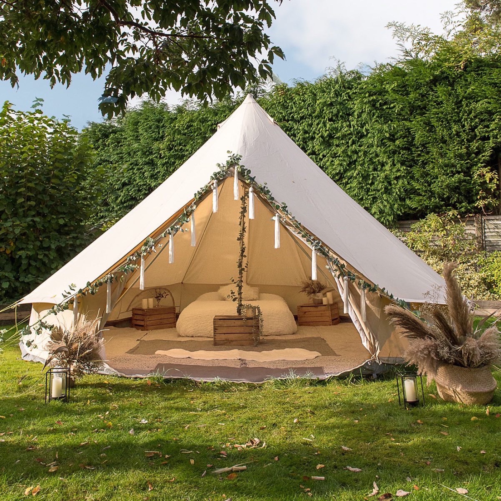 Boho-dressed bell tent open to a garden, eucalyptus and pampas